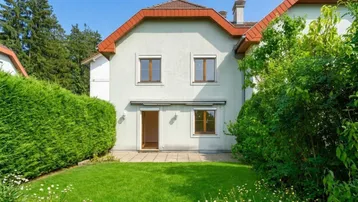 Hinteransicht des Hauses mit gepflegtem Rasen, Hecke und Zugang zur Terrasse.