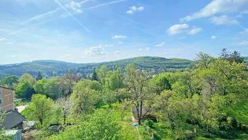 Weitläufiger Panoramablick über grüne Hügel und bewaldete Landschaft unter blauem Himmel.