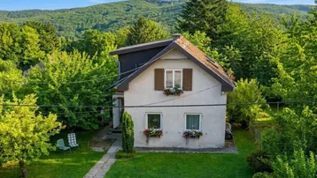 Vorderansicht eines charmanten Einfamilienhauses mit grüner Umgebung und Bergblick unter blauem Himmel.