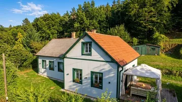 Charmantes Landhaus mit grünen Fensterläden und Holzdach in idyllischer Hügellandschaft.