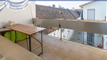 Balkon mit Fliesenboden, Metallgeländer und Blick über die Dächer.