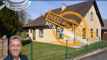 Einfamilienhaus mit gepflegtem Vorgarten und Zaun, umgeben von grüner Landschaft.