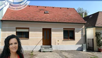 Einfamilienhaus mit Putzfassade und Ziegeldach, umgeben von einer kleinen Grünfläche.