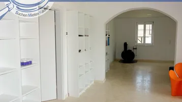 Heller Wohnbereich mit Regalen, Kaminofen und gefliestem Boden, offen gestaltet.