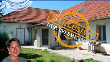 Hausrückseite mit gepflasterter Terrasse und Gartenbereich, teilweise überdacht, mit Blick ins Grüne.