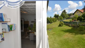 Blick von einem Balkon auf eine grüne Hügellandschaft mit Bäumen und Wohnhäusern.