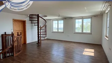 Geräumiger, heller Raum mit Holzboden, Wendeltreppe und weitem Ausblick durch die Fenster.