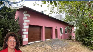 Rosa gestrichenes Haus mit zwei Garagentoren und einem Turm, umgeben von Bäumen.