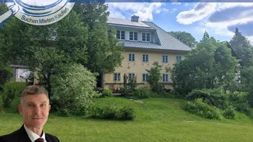 Großzügiges Anwesen mit gelber Fassade, umgeben von viel Grün und Bäumen, mit einem Herrn im Vordergrund.