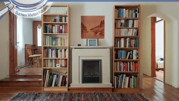 Gemütlicher Raum mit Kamin, Bücherregalen und Teppich, ideal als Lese- oder Wohnzimmer.