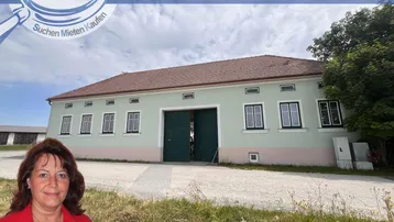 Ländliches Gebäude mit hellgrüner Fassade und rotem Ziegeldach unter bewölktem Himmel.