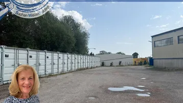 Großer Schotterplatz mit Lagercontainern und einem Gebäude im Hintergrund unter blauem Himmel.