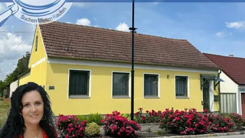 Gelbes Einfamilienhaus mit rotem Ziegeldach und blühenden Rosen im Vorgarten.