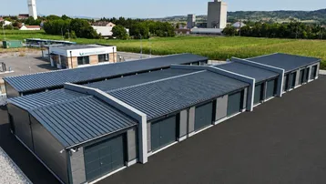 Luftaufnahme eines modernen Lagerkomplexes mit mehreren Garagen und umliegenden Feldern unter blauem Himmel.