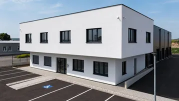 Modernes weißes Bürogebäude mit dunklen Fenstern und einem Parkplatz mit barrierefreiem Zugang.