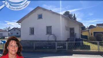 Einfamilienhaus mit weißer Fassade und Steinsockel, umgeben von einem kleinen Vorgarten.
