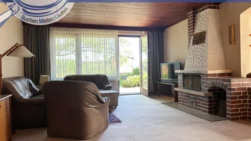Gemütliches Wohnzimmer mit Kamin, Ledersofas und Zugang zum Garten.