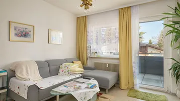 Helles Wohnzimmer mit gemütlichem Sofa, Teppichboden und direktem Zugang zum Balkon.