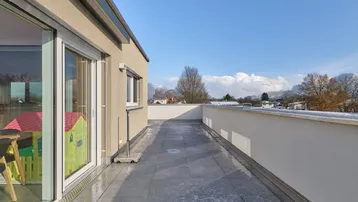 Geräumige Dachterrasse mit Fliesenboden und weitem Blick auf die Umgebung und die Berge.