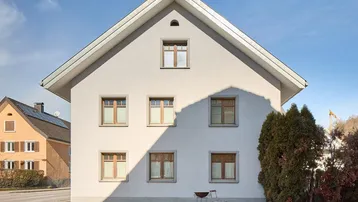 Helle Fassade eines Einfamilienhauses mit Satteldach und Holzfenstern.
