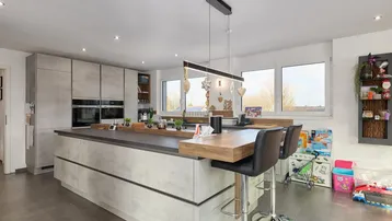 Moderne Küche mit großer Kücheninsel, integrierten Geräten und viel Tageslicht durch große Fenster.