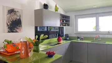 Moderne Küche mit leuchtend grünen Arbeitsplatten, grauen Schränken und großem Fenster.