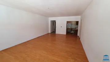 Geräumiges Wohnzimmer mit hellem Parkettboden und offenem Zugang zu einer separaten Küche.