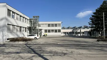 Außenansicht eines modernen Bürogebäudes mit großem Parkplatz und externem Aufzug.