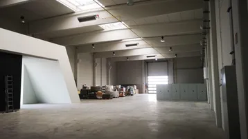 Geräumige Lagerhalle mit hohen Decken, Betonboden und Tageslicht durch Oberlichter.