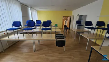 Geräumiger Schulungsraum mit mehreren Tischen und blauen Stühlen, bereit für den Unterricht.