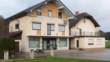 Gebäudeansicht mit teilweise verputzter Fassade und sichtbaren Ziegeln im oberen Bereich.