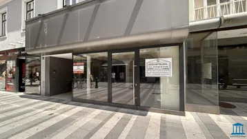 Moderne Geschäftsfassade mit großen Schaufenstern und Vermietungsschildern an einer belebten Straße.