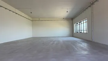 Großer, leerer Raum mit Betonboden und Fenstern, ideal für Lager oder Werkstatt.