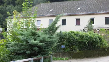 Das Gebäude ist von üppigem Grün umgeben und zeigt eine einfache Fassade mit mehreren Fenstern.