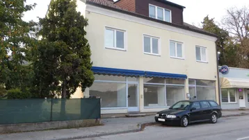 Ansicht des Gebäudes von der Straße mit einer blauen Markise und einem geparkten Auto davor.
