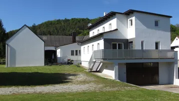 Ansicht des Wohnhauses mit angrenzendem Nebengebäude, Balkon und großem Gartenbereich.