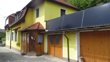 Gelbes Haus mit rotem Ziegeldach, integrierter Garage und Solarpaneelen auf dem Dach.
