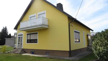 Rückseite des gelben Hauses mit Balkon und grünem Rasen.