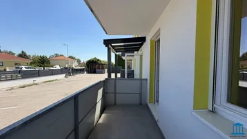 Heller Balkon mit Fliesenboden und Überdachung, bietet Blick auf den Parkplatz und die Umgebung.