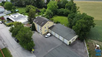 Luftaufnahme eines gelben Gebäudes mit angrenzender Lagerhalle und Parkplatz, umgeben von Grünflächen und Feldern.