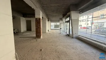 Geräumiges Ladenlokal im Rohbau mit Betonboden, tragenden Säulen und großen Fenstern zur Straßenseite.