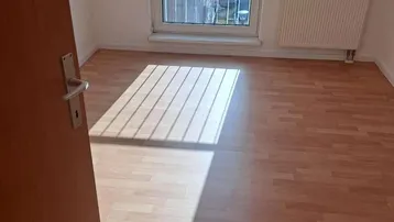 Helles Zimmer mit Laminatboden, Heizkörper und Zugang zu einem französischen Balkon.