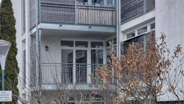 Modernes Mehrfamilienhaus mit mehreren Balkonen und Holzverkleidung an der Fassade.