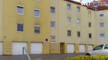 Gelbes Mehrfamilienhaus mit mehreren Garagen im Erdgeschoss und Rollläden an den Fenstern.