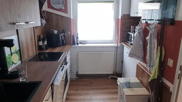 Funktionale Küche mit Holz- und weißen Schränken, Laminatboden und Fenster.