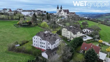 Luftaufnahme einer Wohnsiedlung mit Mehrfamilienhäusern und einer historischen Kirche im Hintergrund.