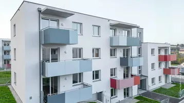 Modernes Mehrfamilienhaus mit farbigen Balkonen und gepflegten Grünflächen in einer ruhigen Umgebung.