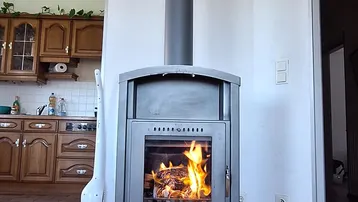 Moderner Holzofen mit brennendem Feuer, der Wärme spendet, mit Blick auf die angrenzende Küche.