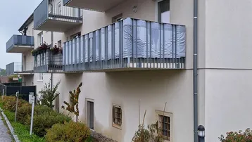 Modernes Mehrfamilienhaus mit mehreren Balkonen und gepflegter Grünanlage im Erdgeschoss.
