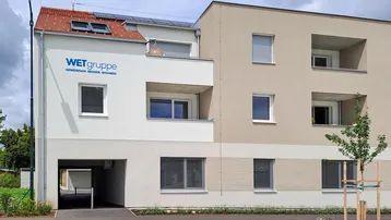 Modernes Mehrfamilienhaus mit heller Fassade, Balkonen und Photovoltaikanlage auf dem Dach.
